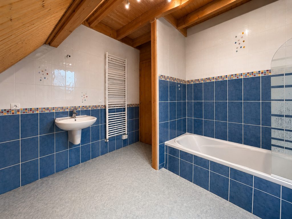 Cette ancienne salle de bains, avec son carrelage bleu et sa baignoire, ne correspondait plus aux envies des occupants. L’objectif : repenser entièrement l’espace tout en conservant l’esprit chaleureux du chalet.